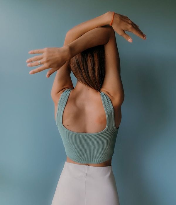 Woman in a graceful yoga pose against a jade green background.